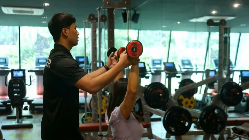 A Personal Trainer in Tenerife Assists a Client with Proper Form During a Weightlifting Exercise